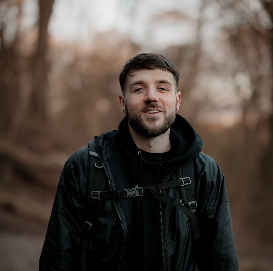 Person in dark clothing posing outdoors against a moody autumn background.