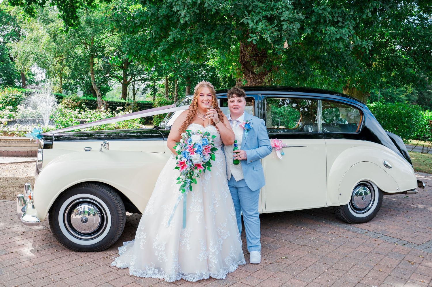 Classic white vintage car parked in a lush garden setting serves as backdrop for an elegant outdoor wedding celebration.