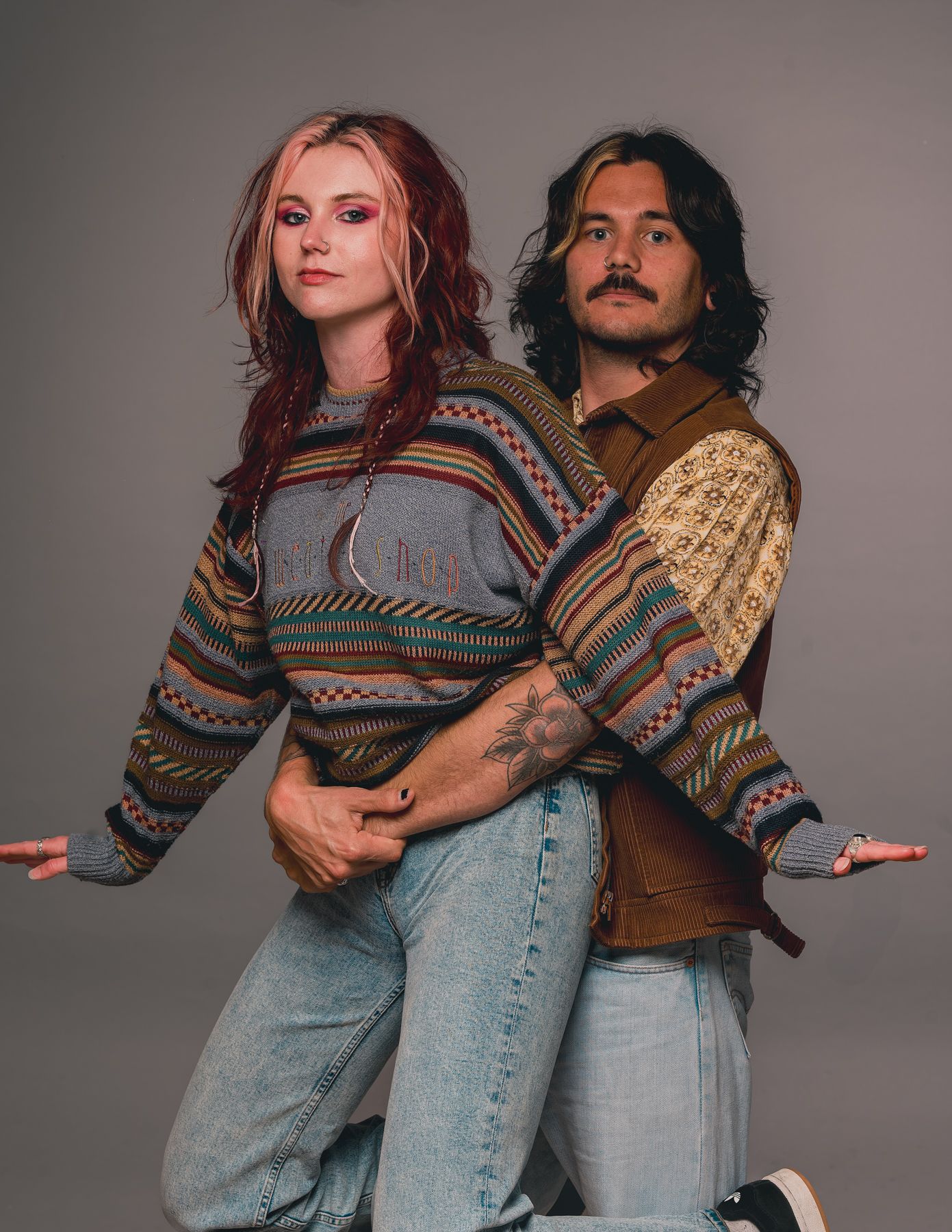 Couple in matching sweaters posing together in studio setting.