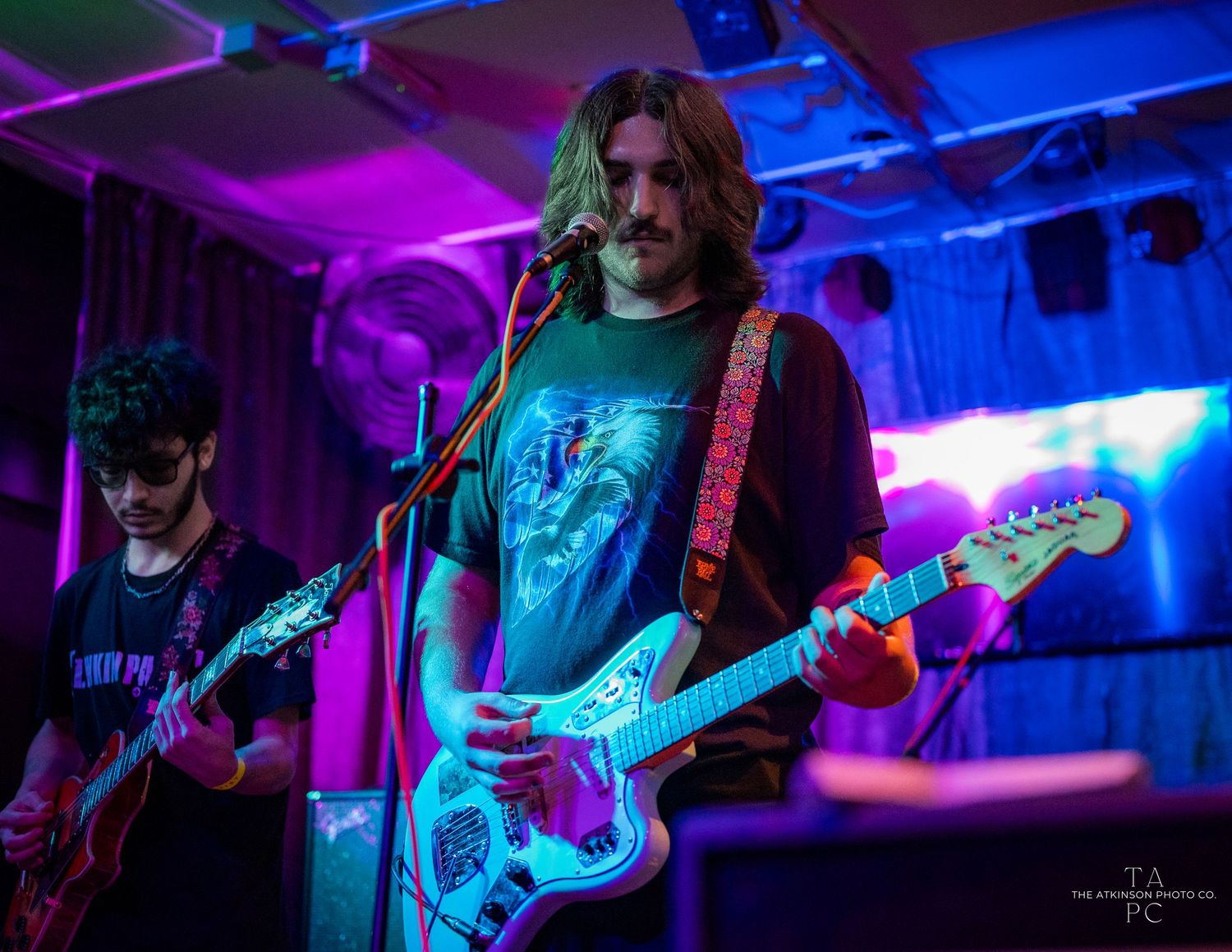 Rock band performing on stage with dramatic blue and purple concert lighting.