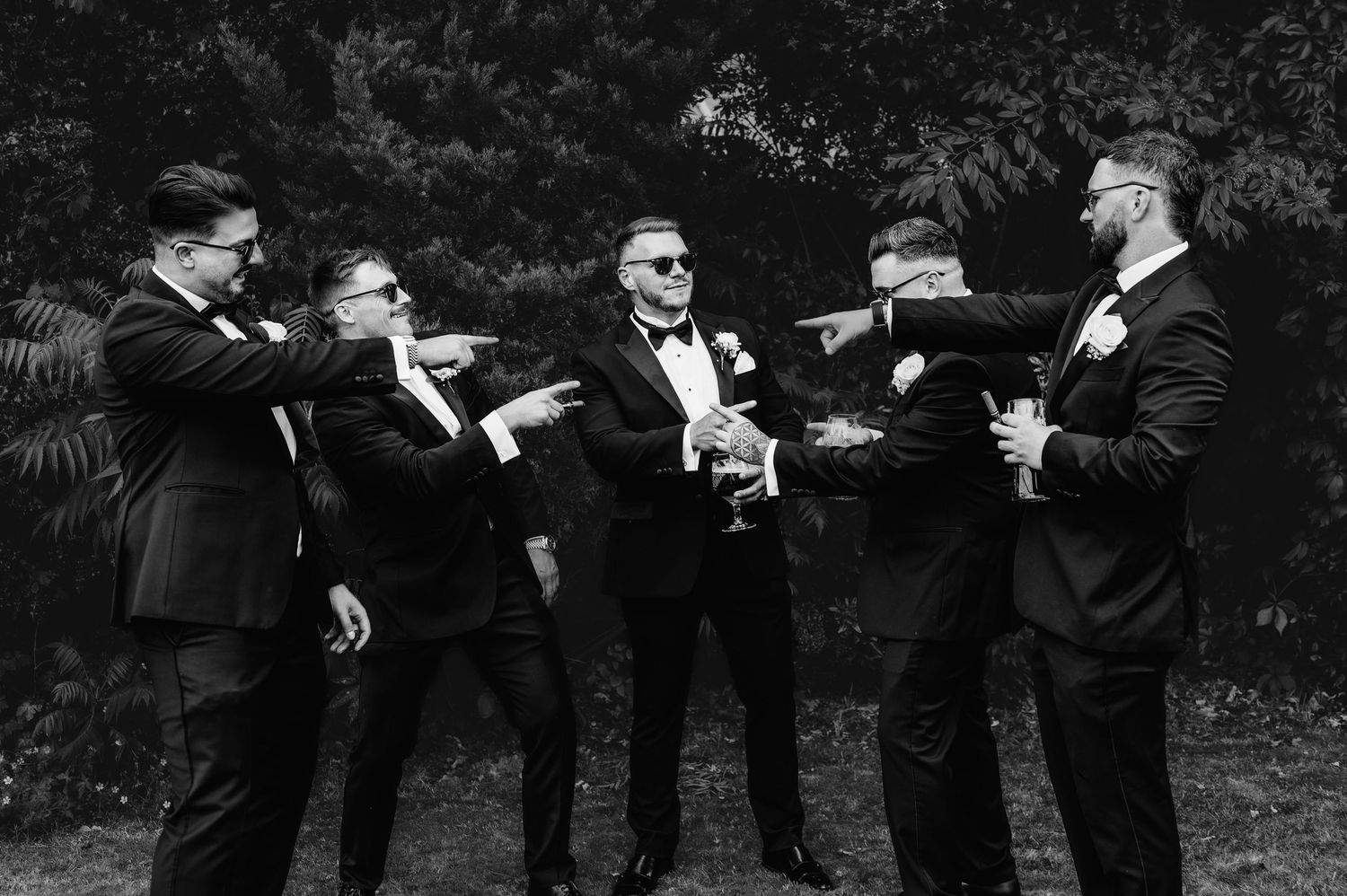Group of men in black tuxedos gathered outside a venue looking at their mobile devices.