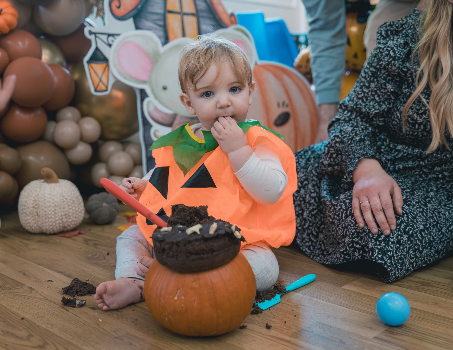 Kids playing with bright orange pumpkins and colorful toys on wooden floor.