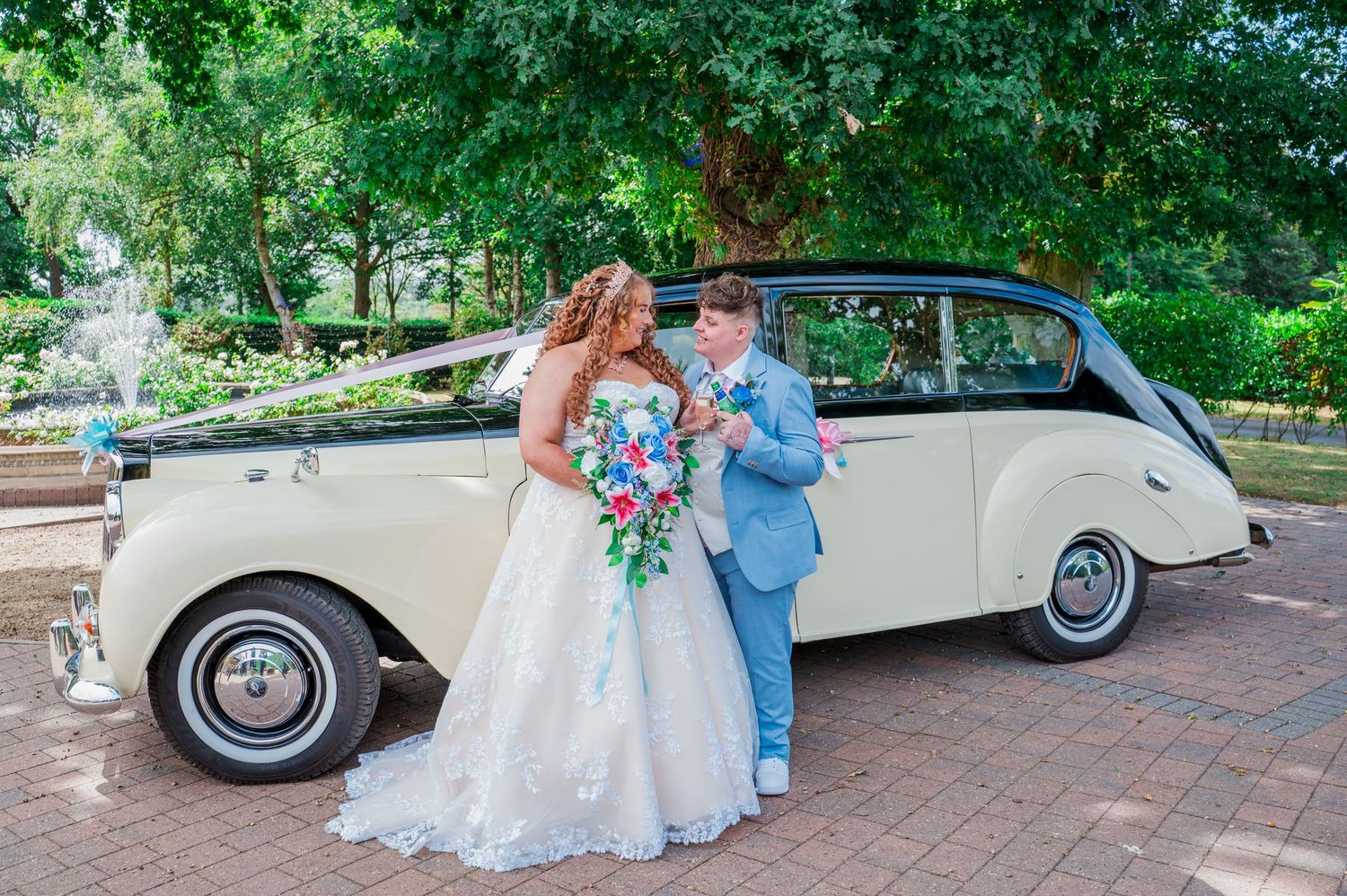 Classic white vintage car parked on brick pathway with floral decorations and wedding party gathering outside.
