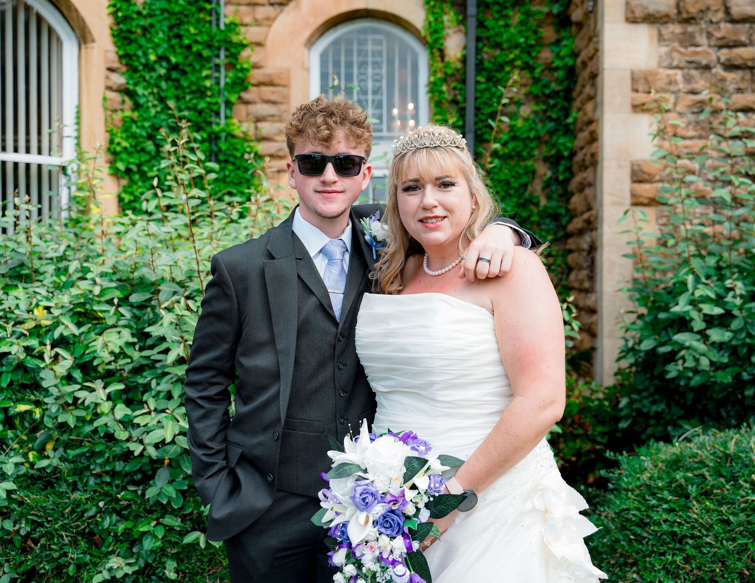 Stylish wedding portraits taken against stone building with ivy covered walls.