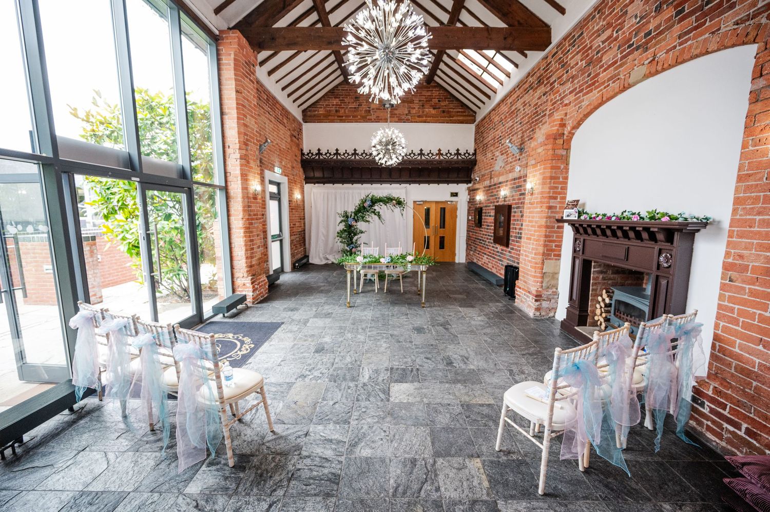 Panoramic view of a rustic brick venue with exposed beams, chandeliers, and stone flooring perfect for events.