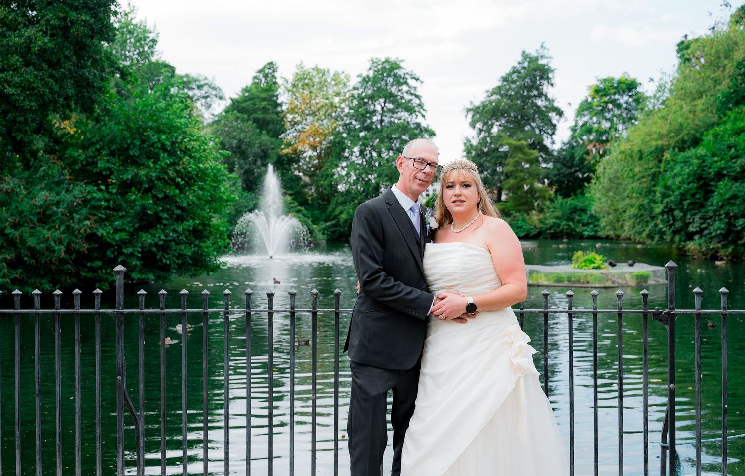 Romantic wedding photo session by a lake with fountain in the background.