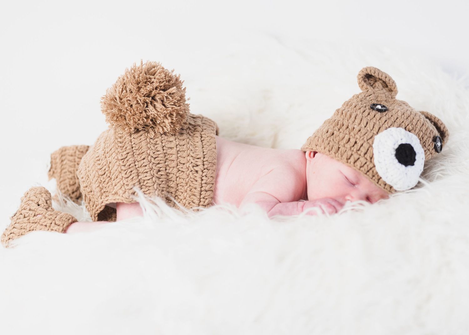 Baby and teddy bear photographed during newborn session on white blanket backdrop.