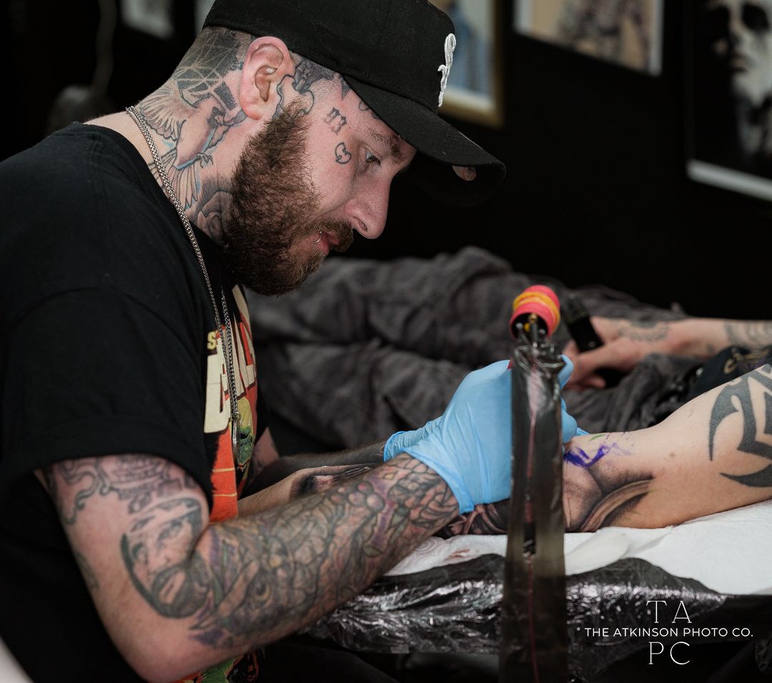 Tattoo artist working on client's arm in professional studio setting.