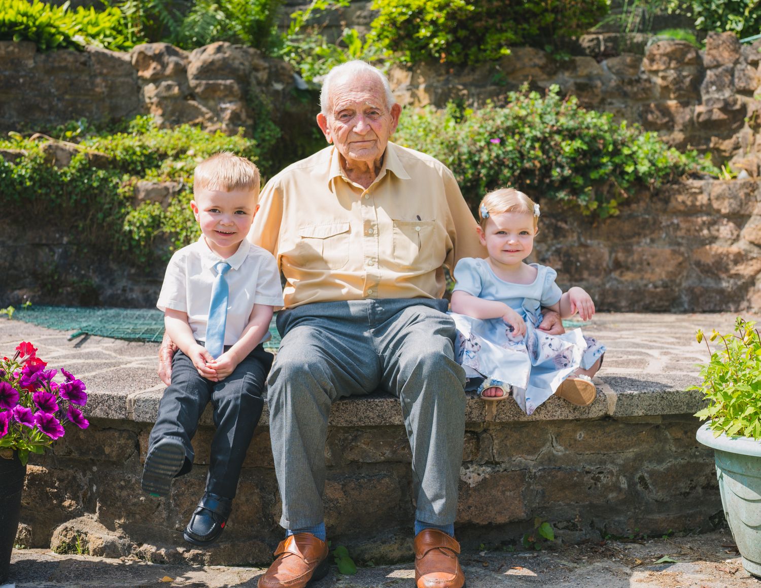 Family members sitting together on stone steps in a sunlit garden setting.