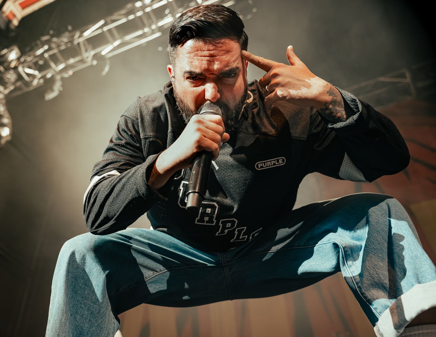 Concert performer singing passionately on stage with dramatic spotlight and dark background.