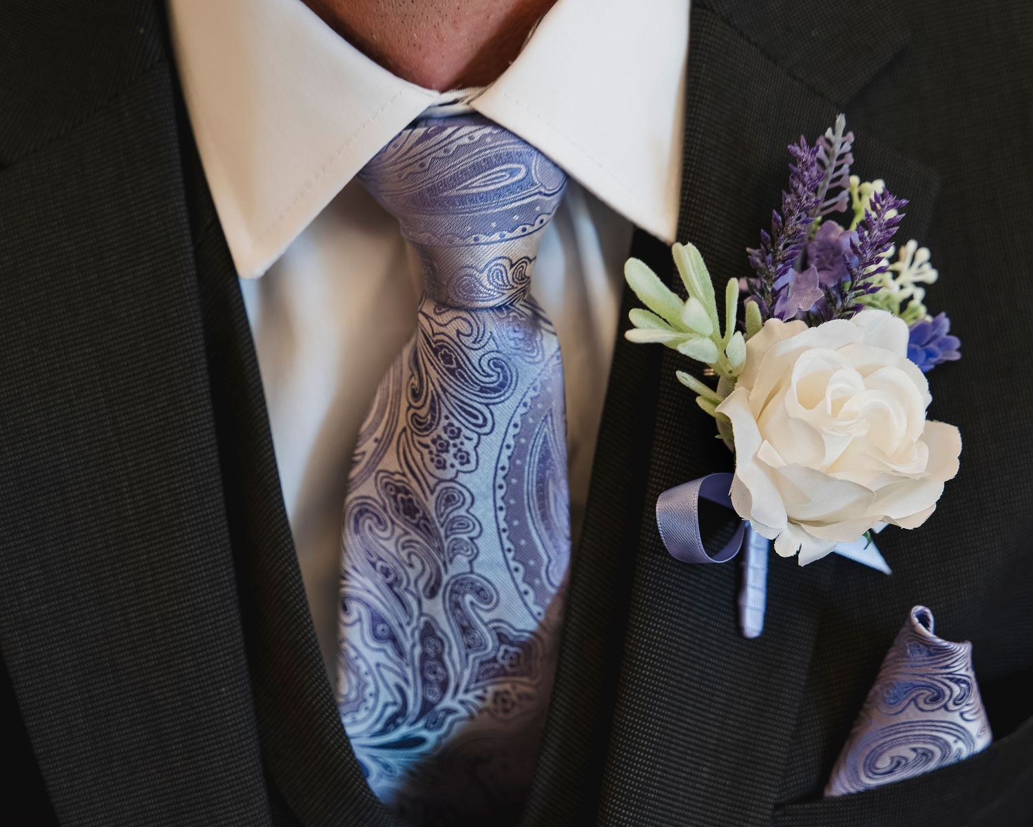 Gray paisley tie with purple boutonniere against a black suit.