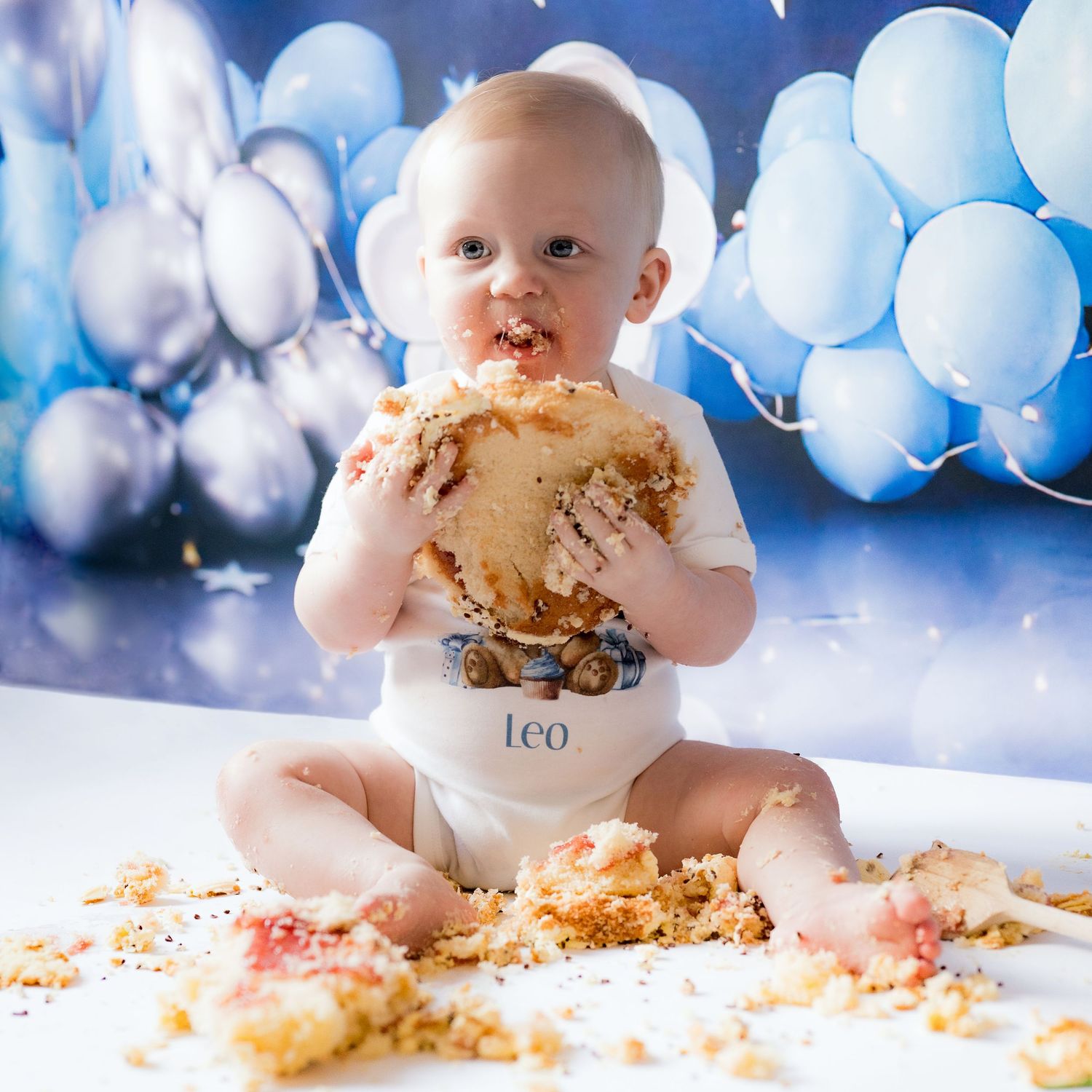 Baby cake smash photo session with blue balloons and messy frosting.
