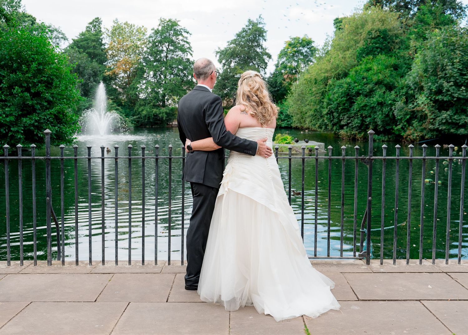 Elegant wedding portraits taken on bridge overlooking water fountain in park.