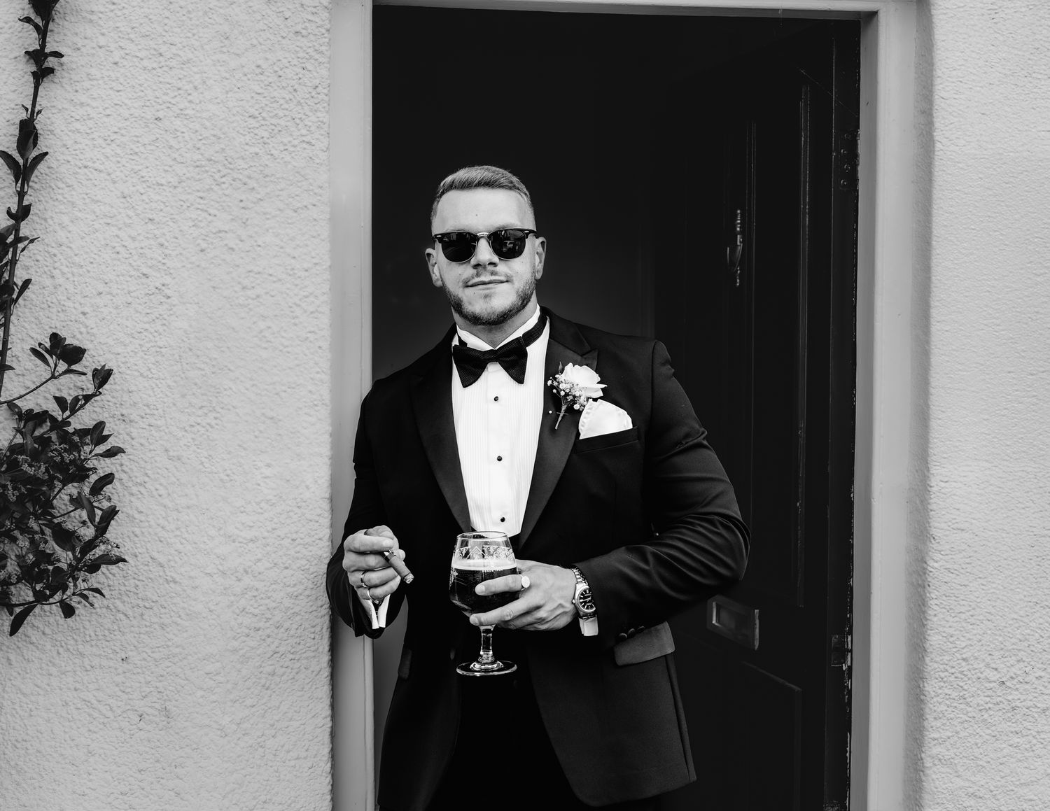 Close-up of men in formalwear looking at mobile phones with sunglasses and boutonnières.