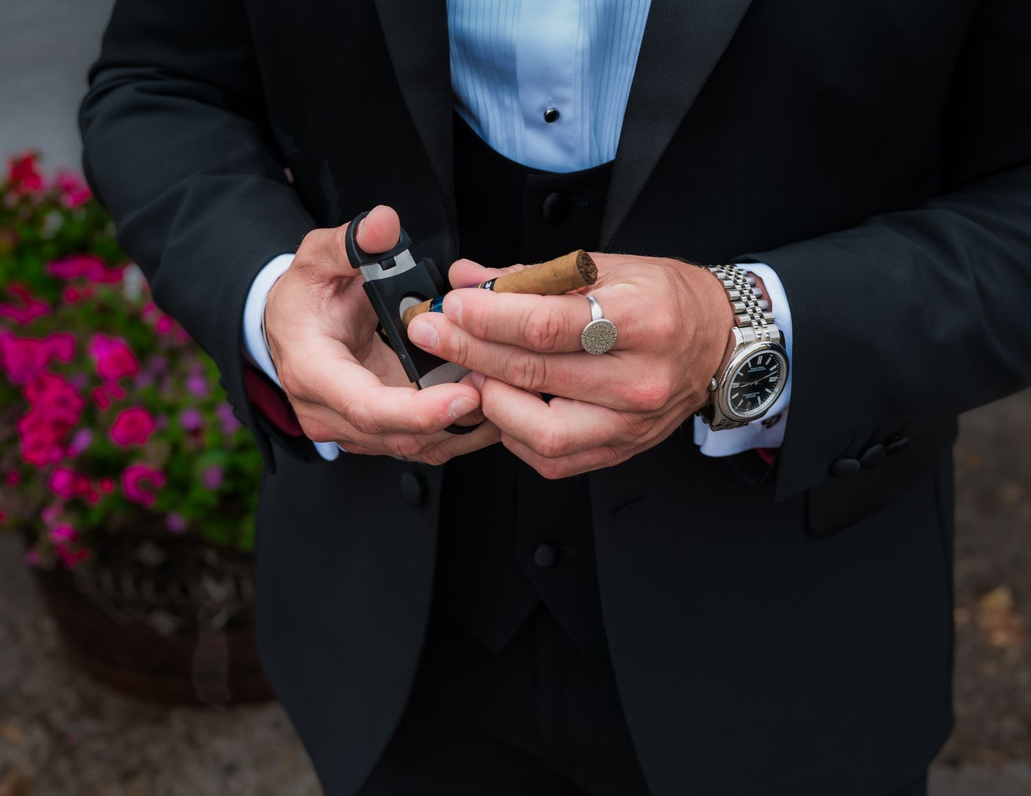 Close-up detail of hands holding phones in formal attire with wedding rings visible.