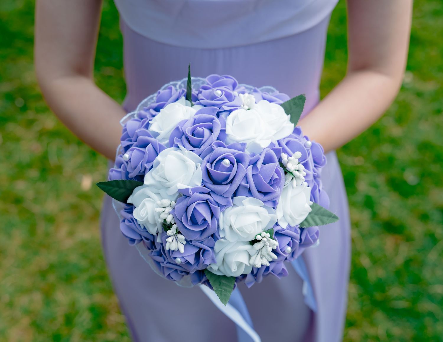 Purple and white rose bouquet held by person in lavender dress.