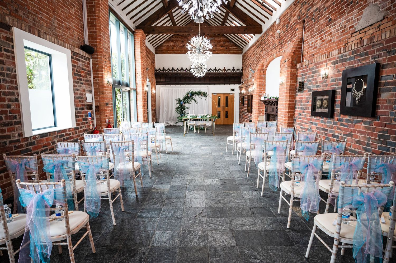 Elegant wedding reception venue with exposed brick walls, crystal chandeliers, and tables decorated with light blue accents.