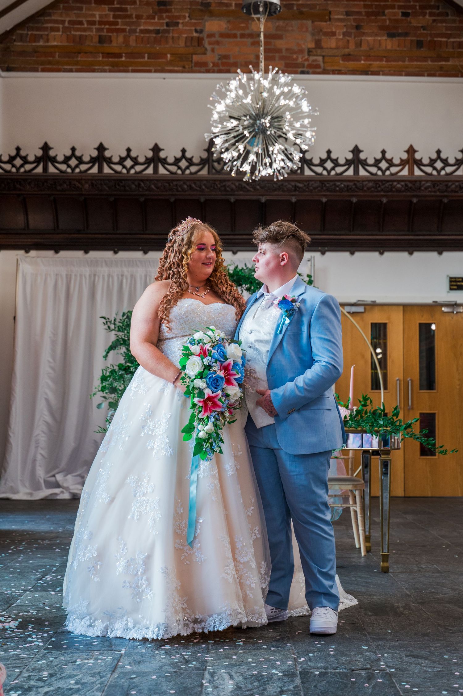 A couple shares a joyful moment at their wedding ceremony under a crystal chandelier with colorful floral bouquet.