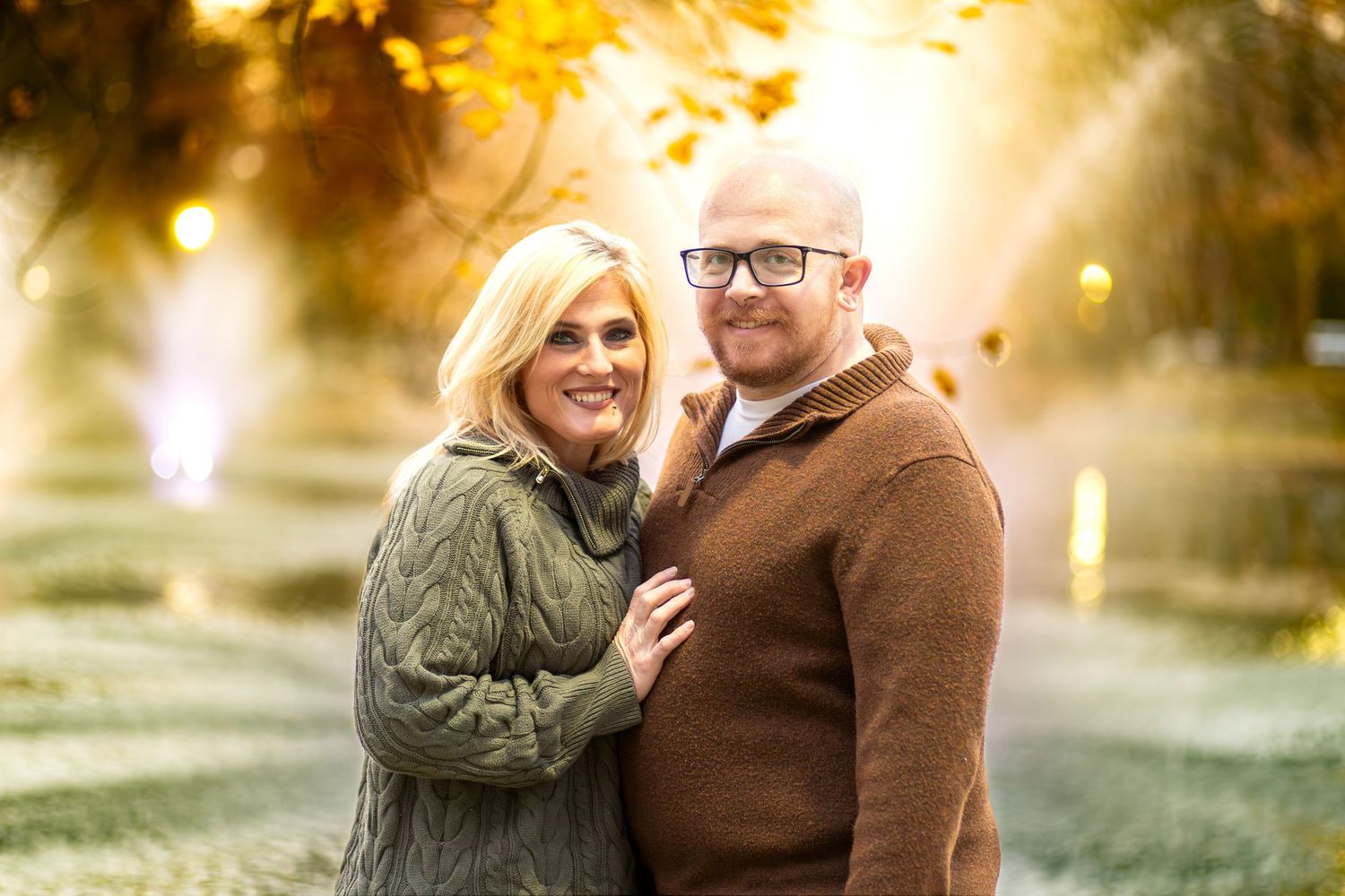 A couple embraces in a romantic autumn setting with golden sunlight filtering through trees in the background.