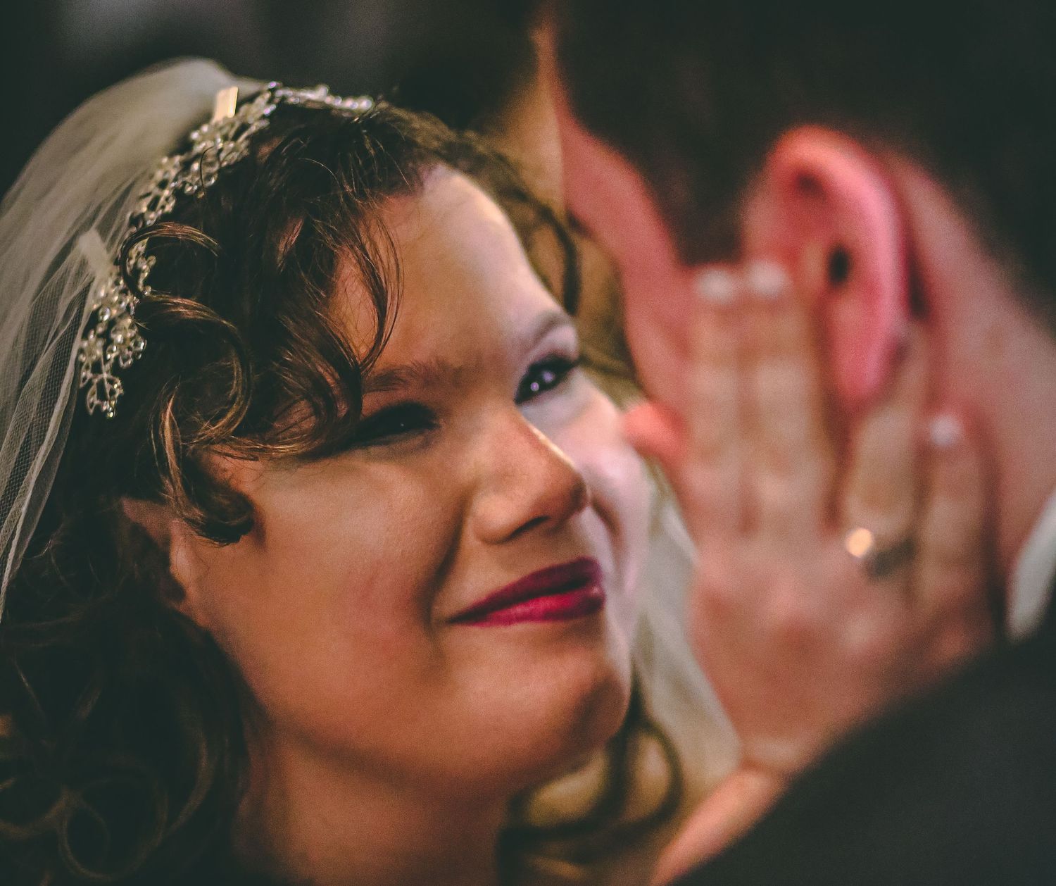 Close-up shot of a smiling bride wearing a delicate tiara and veil during a wedding celebration.