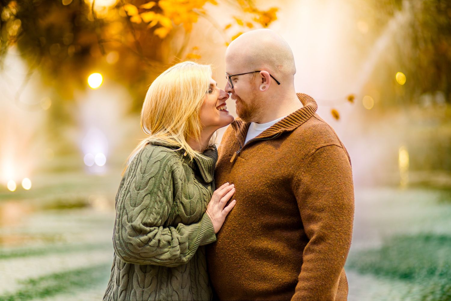 A romantic autumn scene with two people embracing outdoors in warm sweaters as golden sunlight filters through trees.