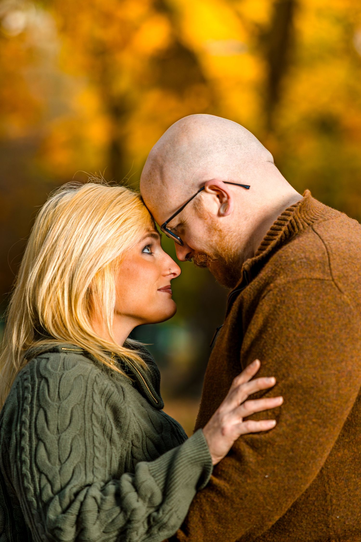 A couple shares an intimate moment in a park during autumn with golden foliage in the background.