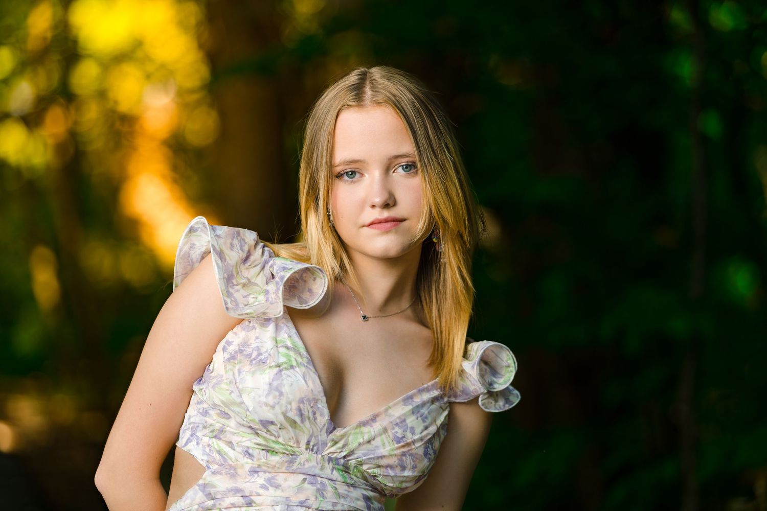 Natural outdoor portrait session in golden sunlight with person wearing white floral blouse against forest background.