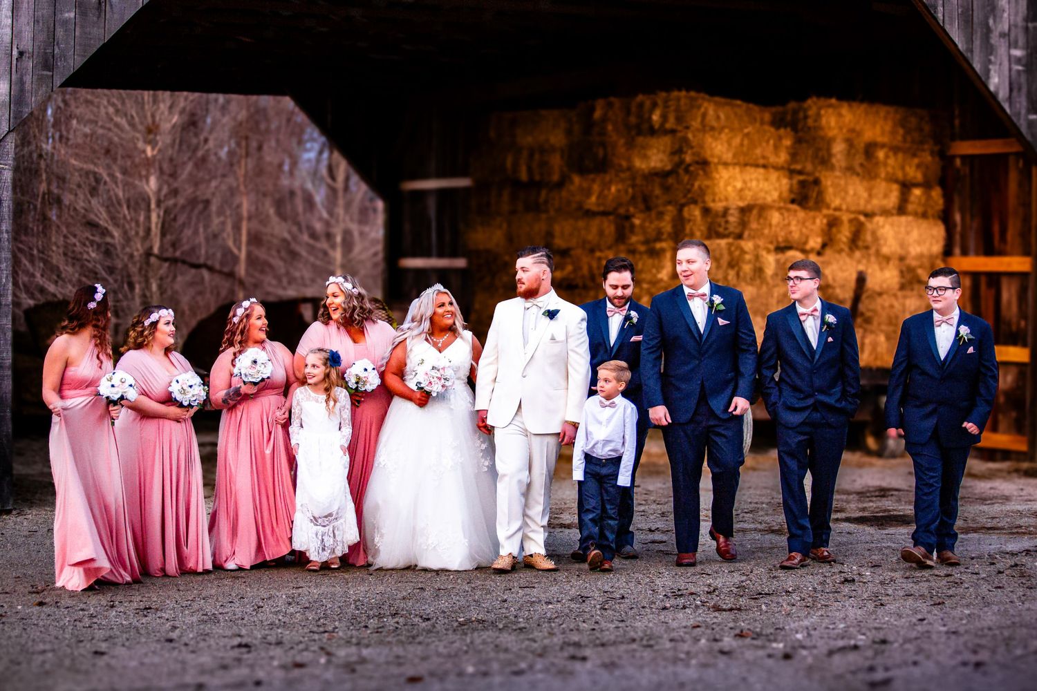 A wedding party in pink bridesmaid dresses and navy suits poses together in front of a rustic stone wall.