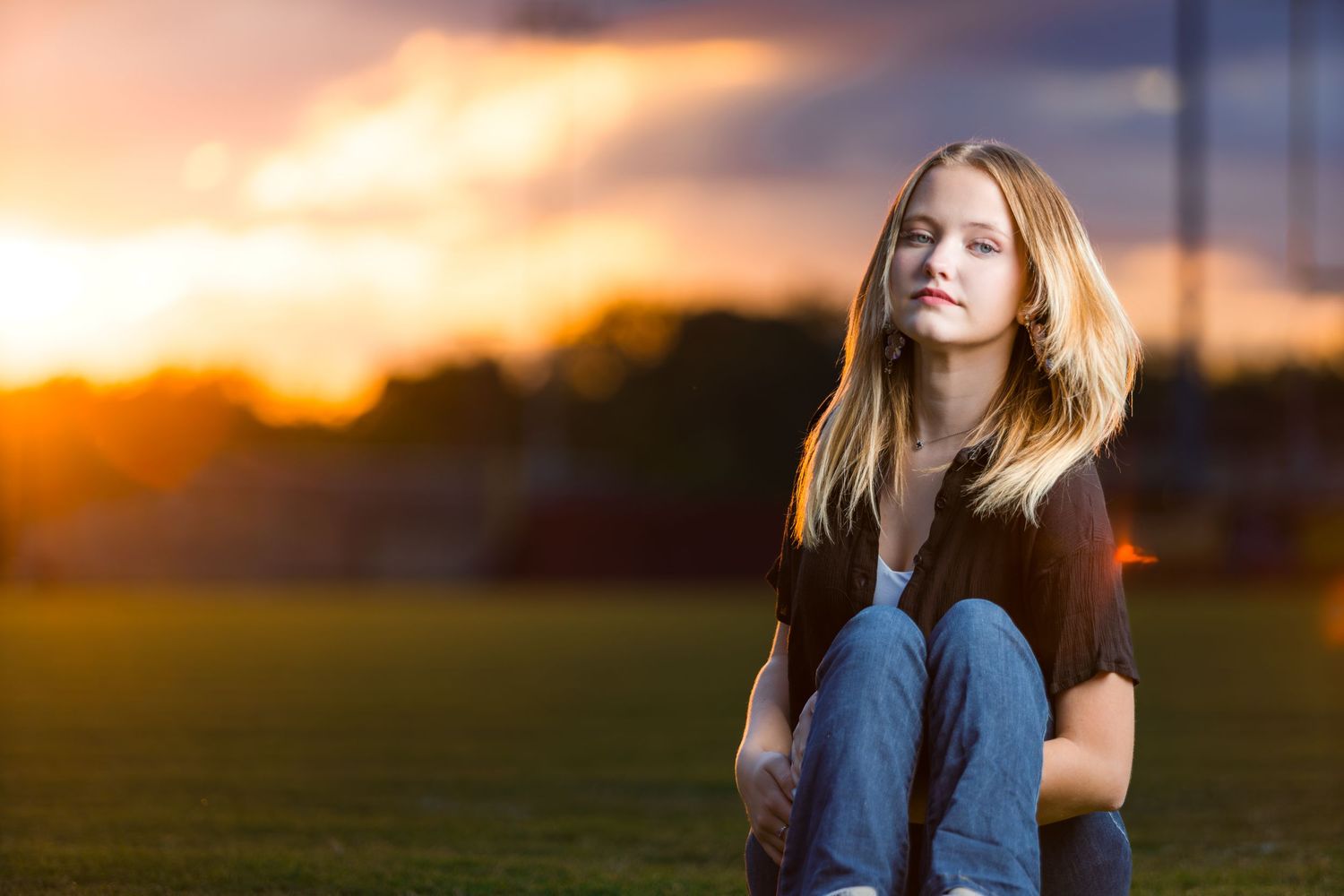 A person stands in silhouette against a vibrant orange sunset sky with golden light streaming through their hair.