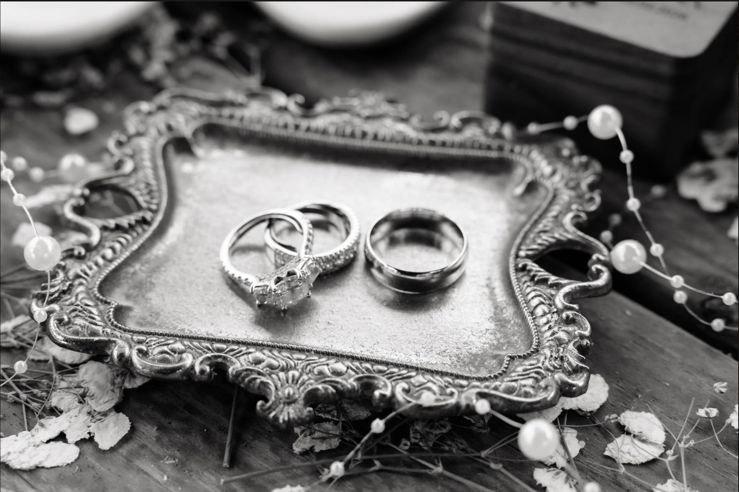 Black and white photo of wedding rings on ornate silver tray.