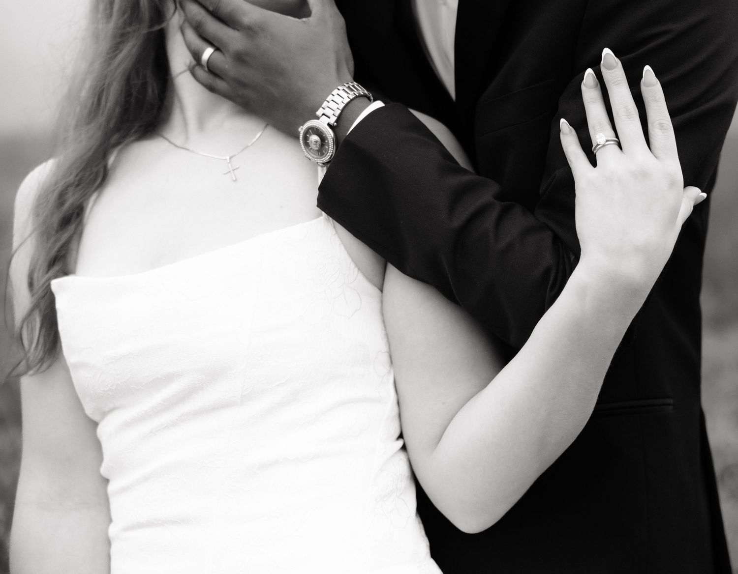 Black and white close-up of bride and groom embracing, showing wedding rings and elegant attire.
