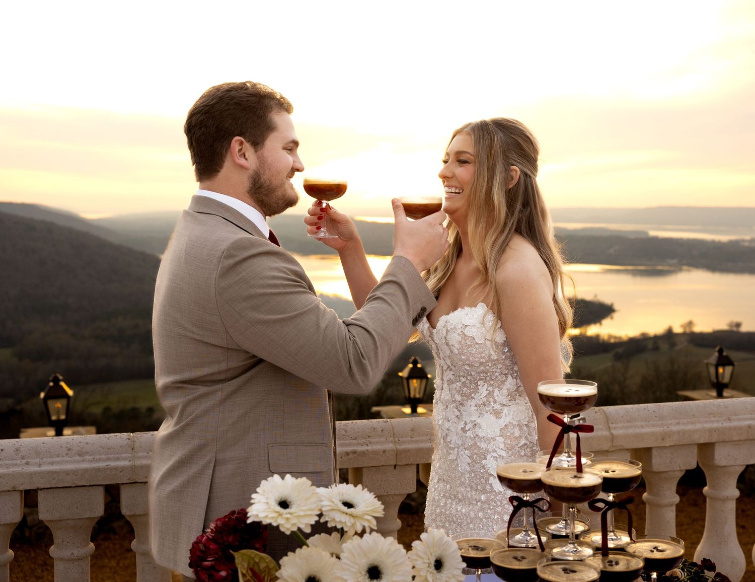 Bride and groom toast with espresso martinis on a balcony at sunset with a stunning lake view.