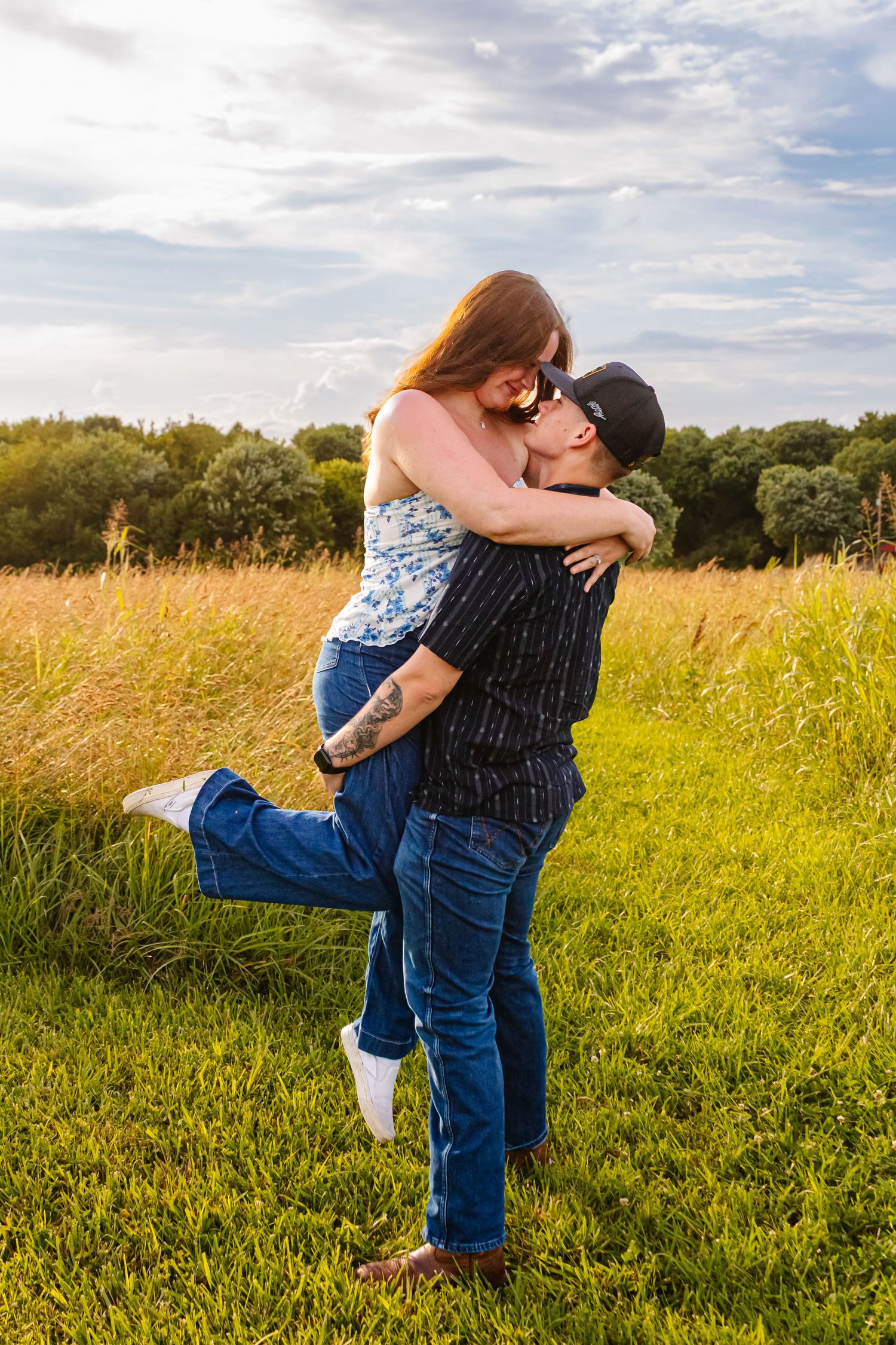 Romantic couple embracing in a sunny green field, man lifting woman during outdoor photo session.