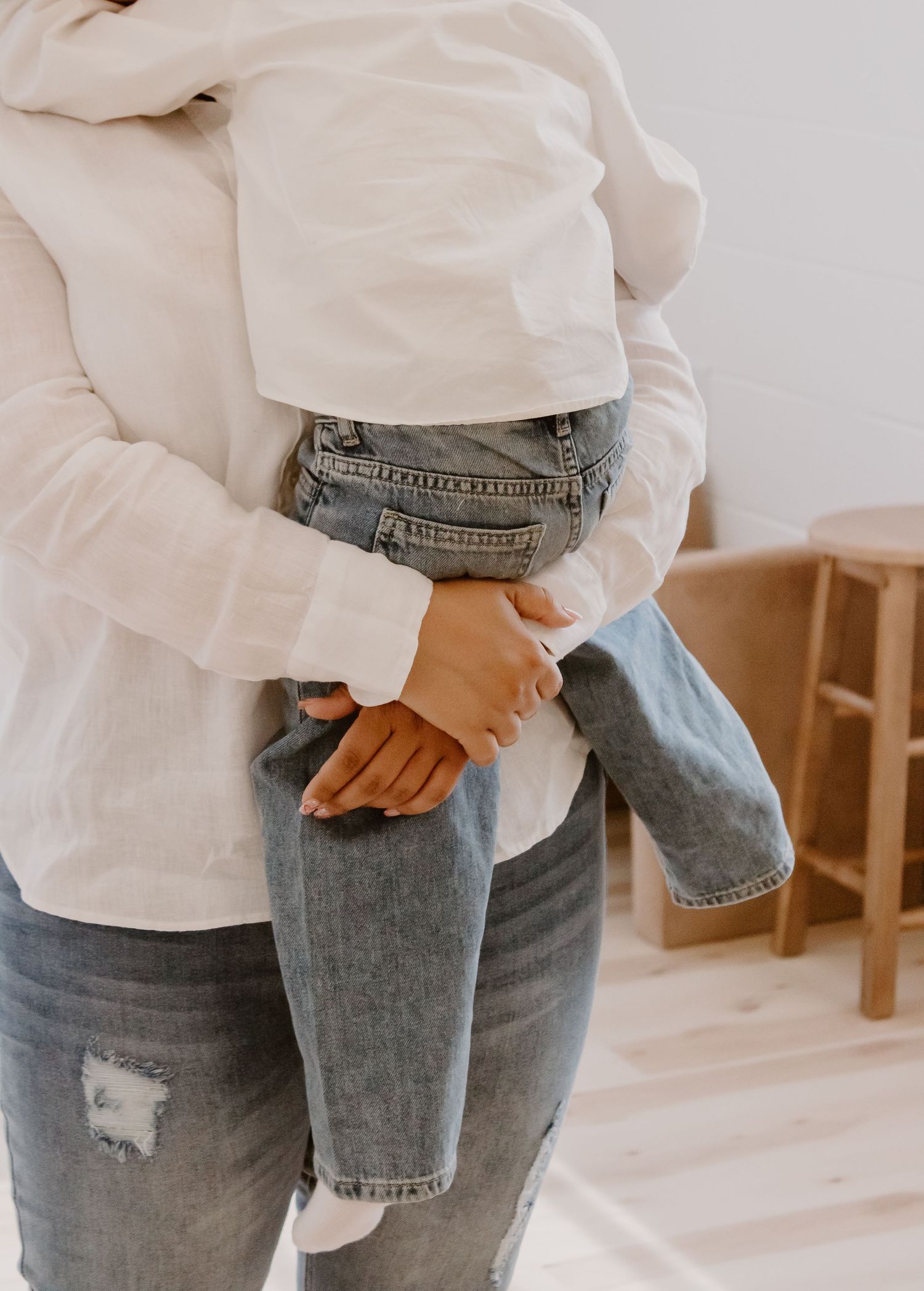 Mother holding young child in denim jeans indoors, close-up of loving parental embrace.