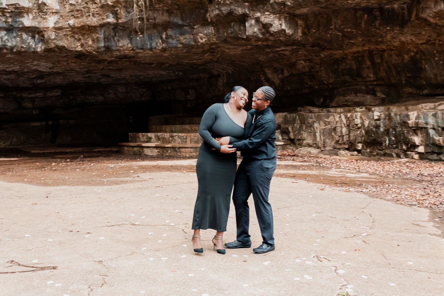 Couple dancing together near a rocky cave entrance during an outdoor engagement photo session.