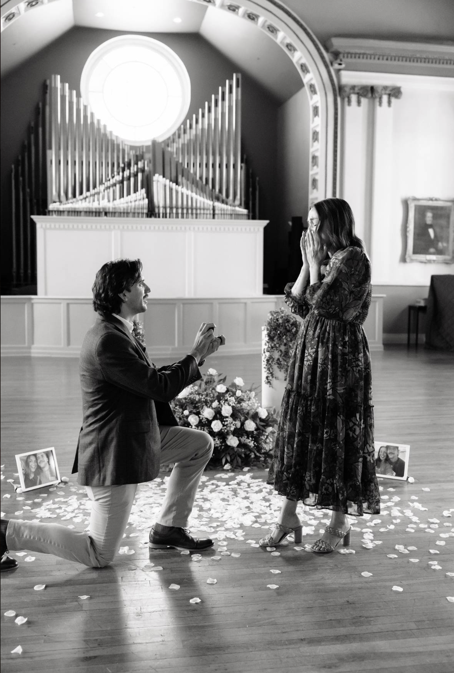 Black and white photo of man proposing on one knee in chapel.