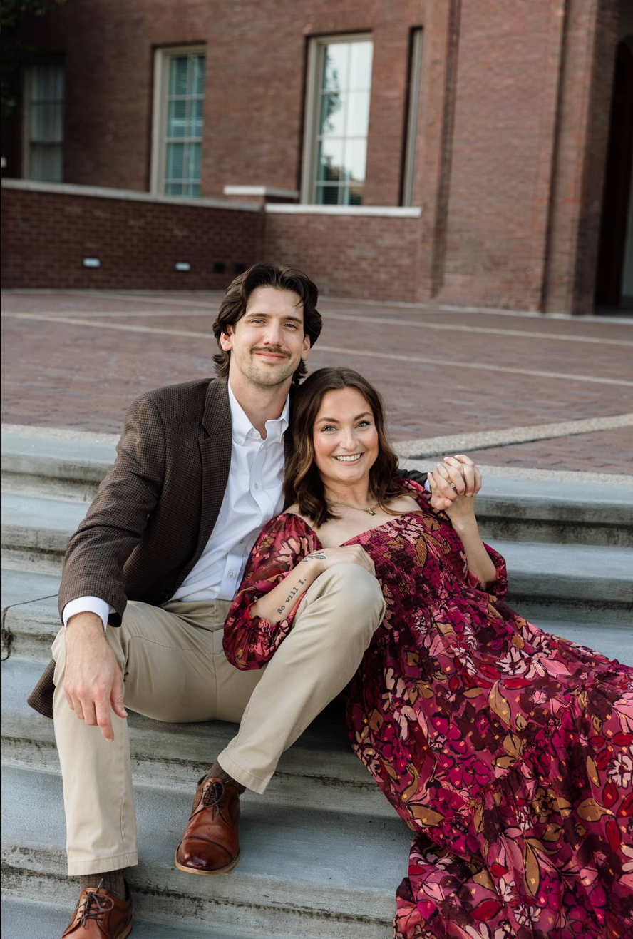 Engaged couple sitting on outdoor steps smiling together.