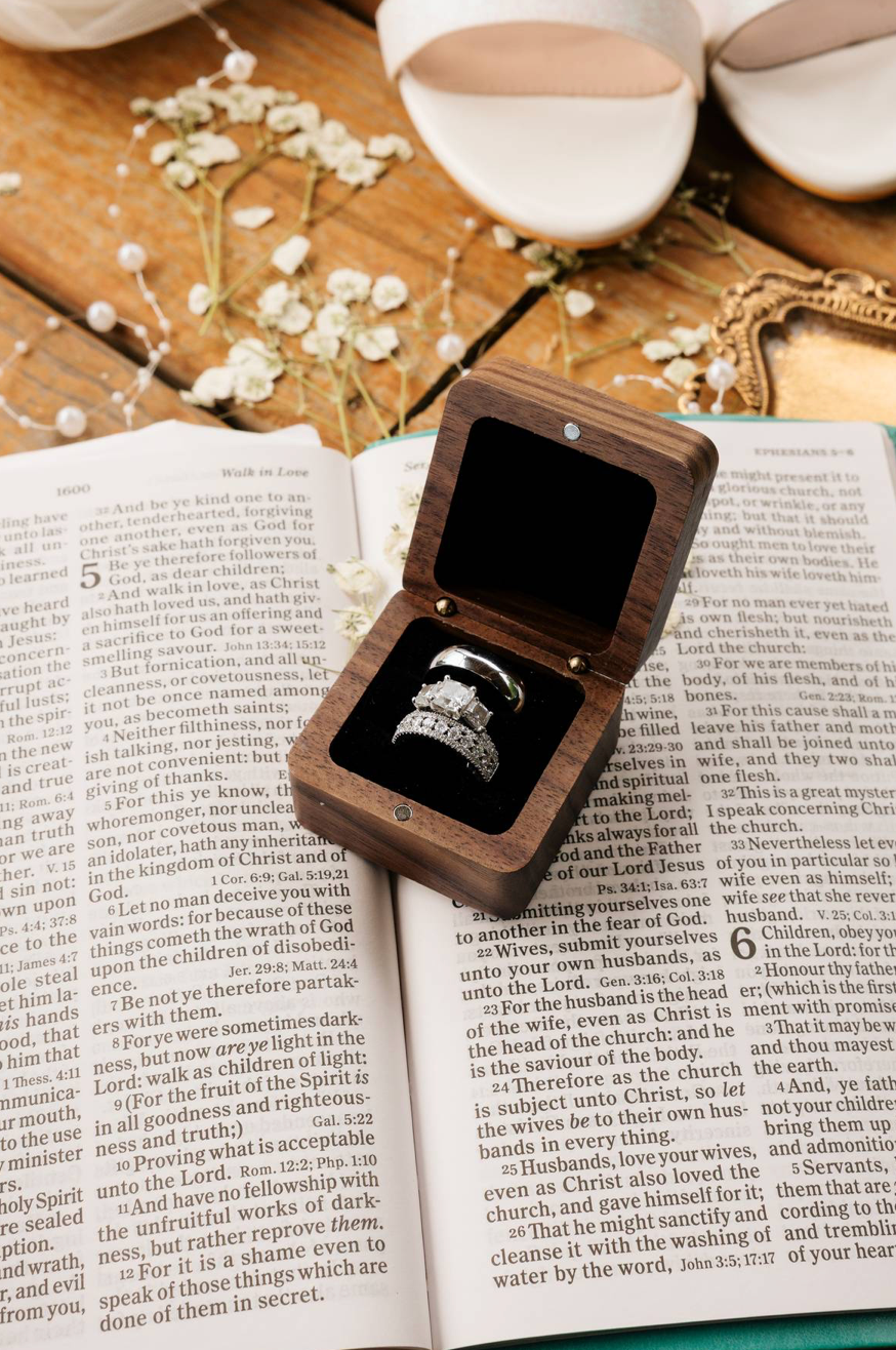 Wedding rings in wooden box on open Bible with floral accents.