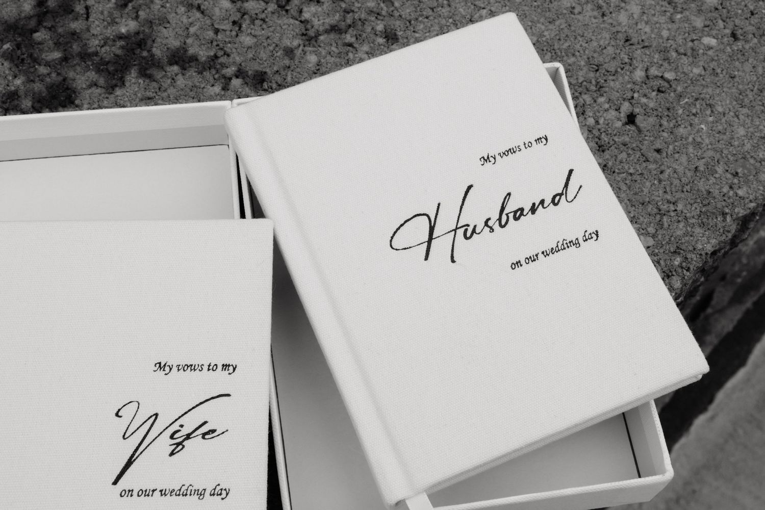 Two elegant white wedding vow books labeled My Vows to My Husband and My Vows to My Wife on a wedding day.