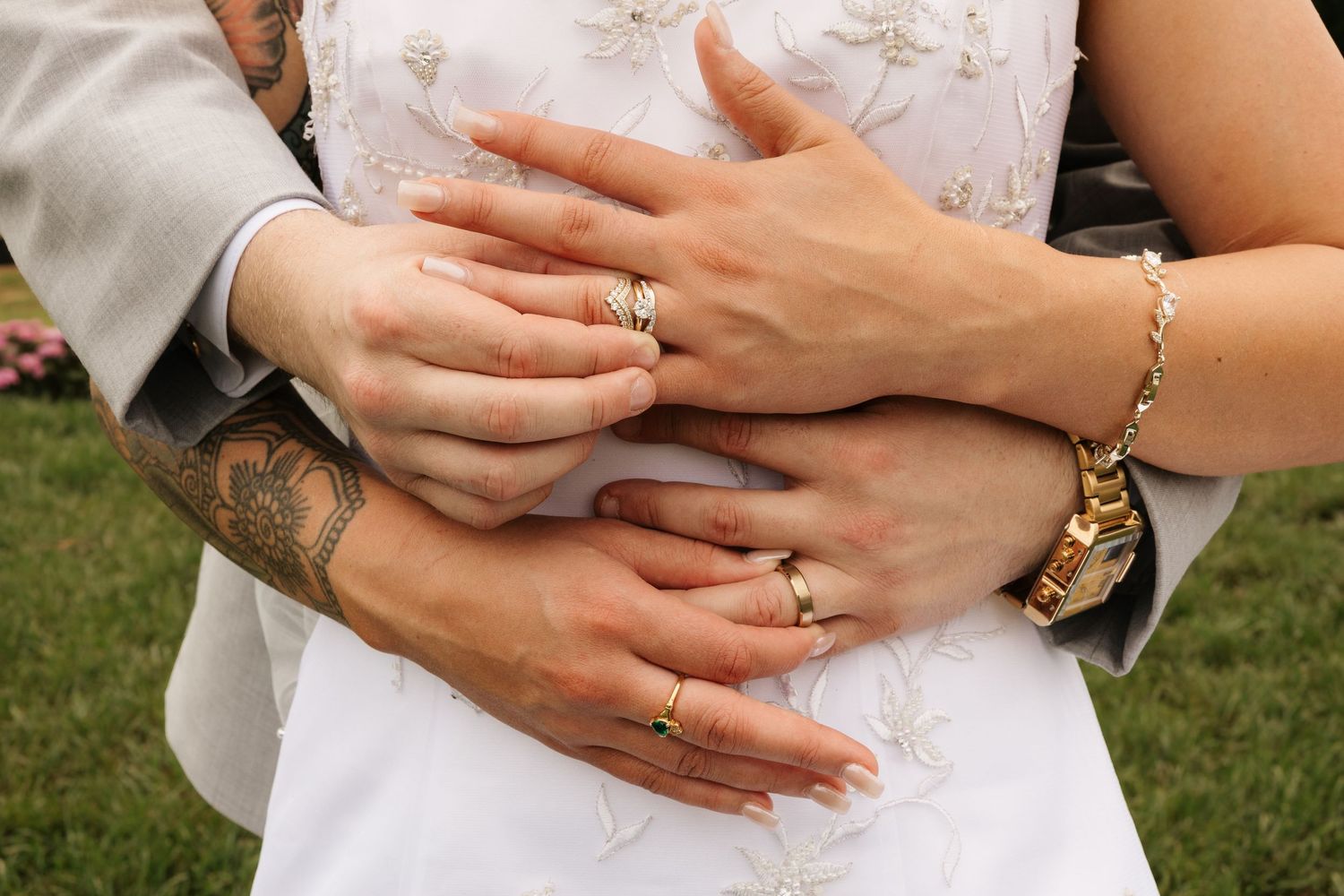 Newlyweds embrace showing gold wedding rings, a tattooed arm, and a gold bracelet watch on a wedding day.