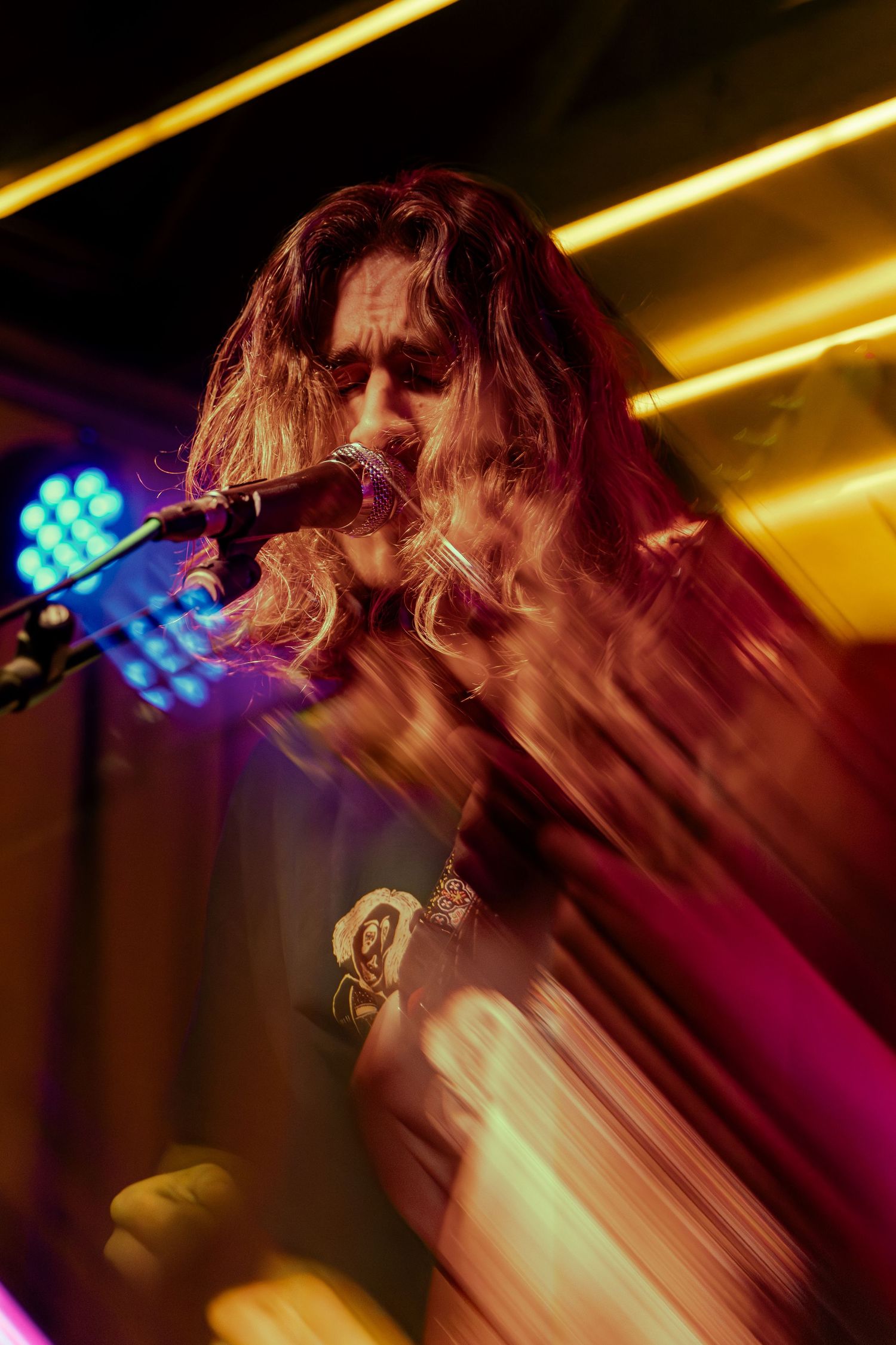 Dynamic concert photo showing performer singing at microphone with motion blur and golden stage lighting effects.