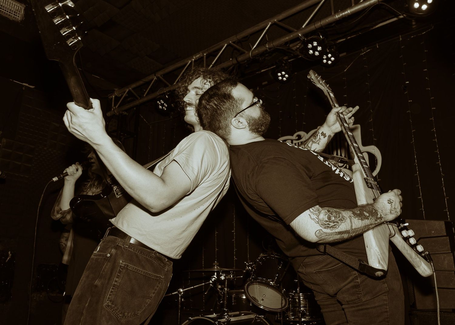 Intense rock concert performance captured in sepia tones showing energetic musicians playing on stage.