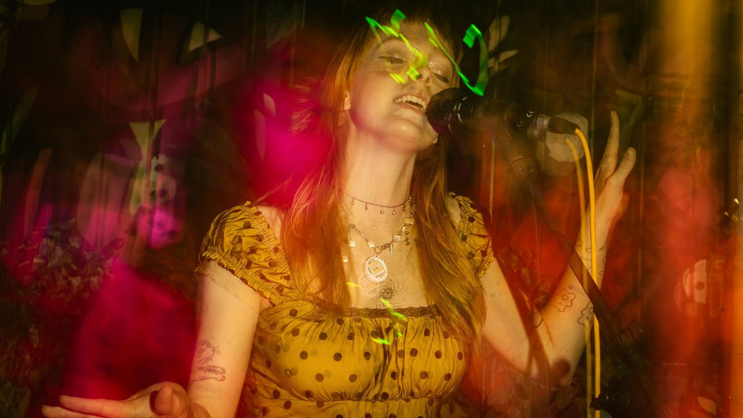 Singer in polka dot dress performs under vibrant red and pink stage lighting.