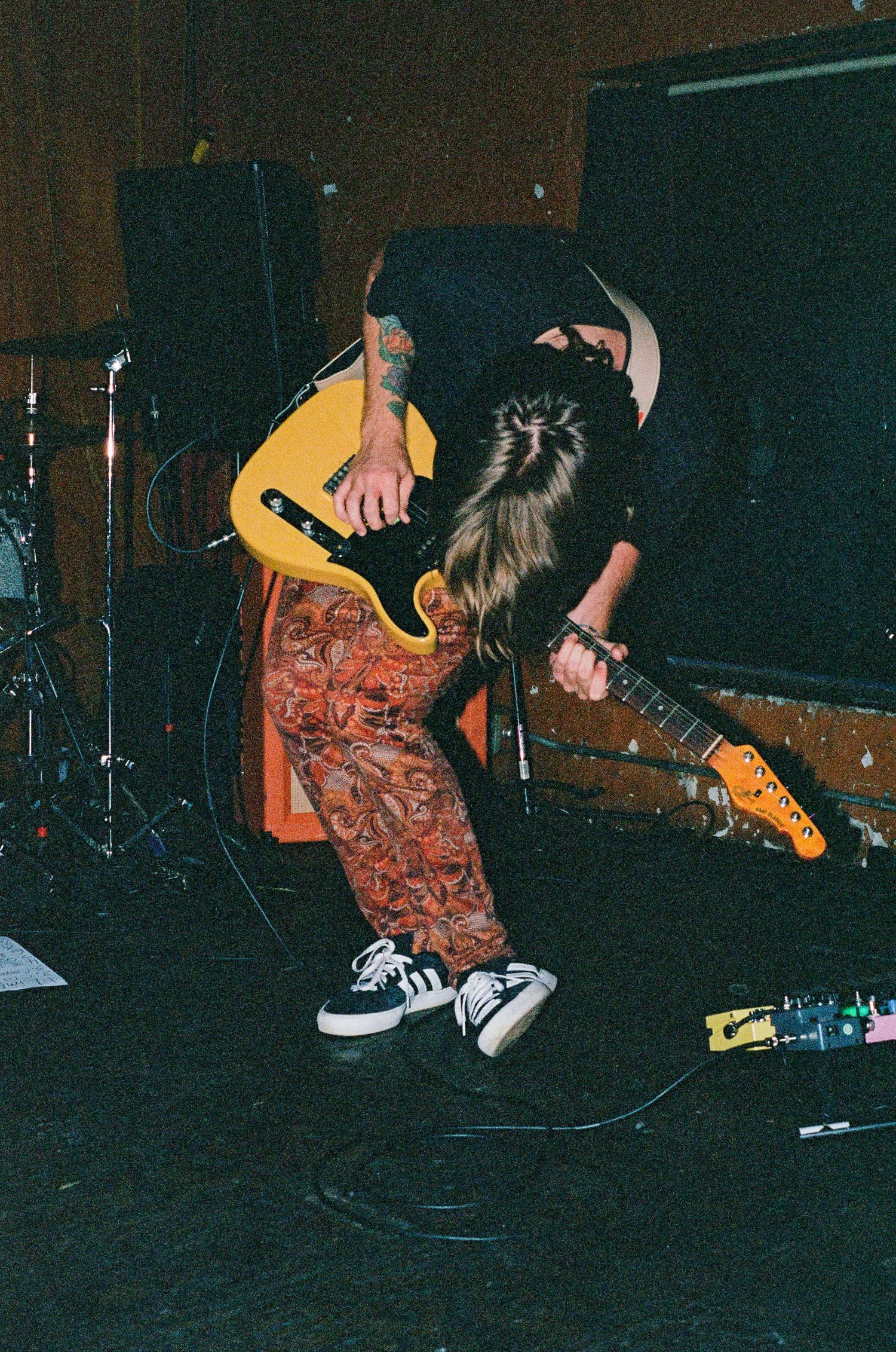 Rock musician playing yellow guitar while bending backwards on dark stage.