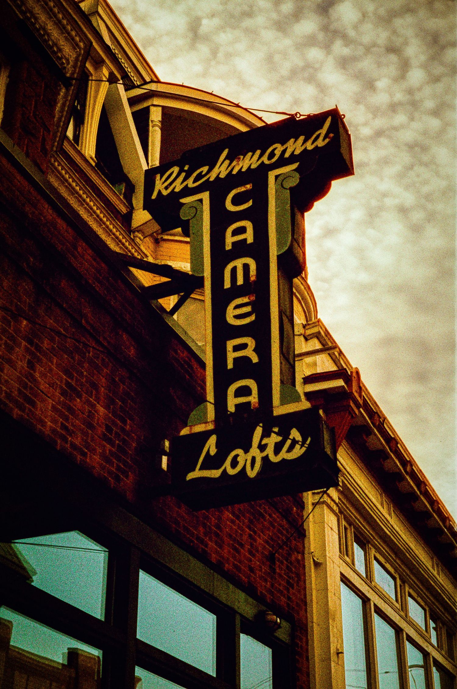 Vintage neon signs for Richmond cafes illuminate brick buildings against a moody evening sky.