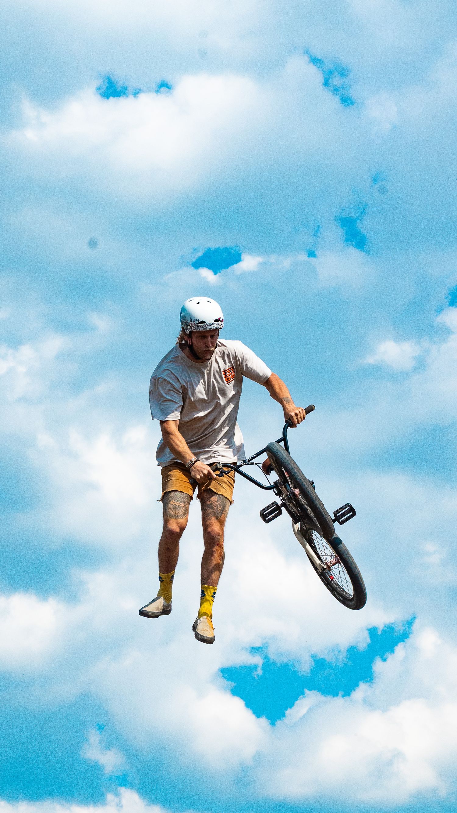 BMX rider and bike soar through air during impressive jump trick against cloudy backdrop.