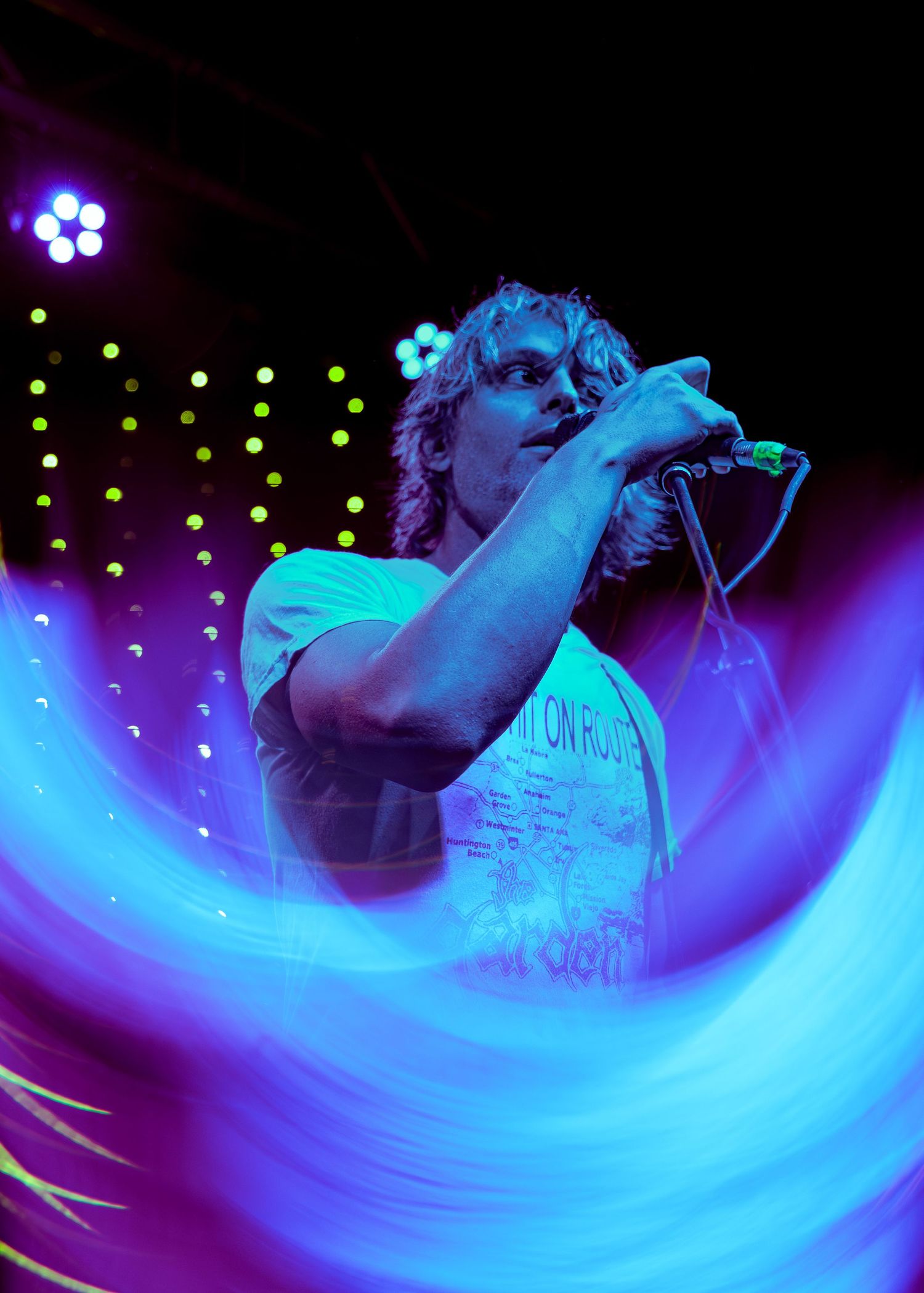 Blue light trails create neon streaks across a dark concert stage during an energetic performance.
