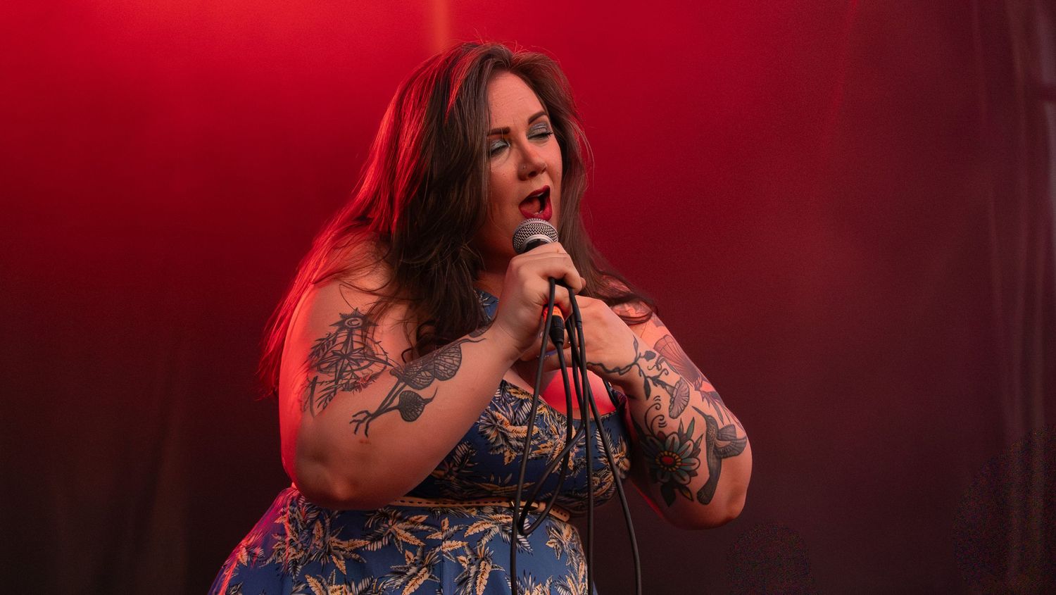 Singer performs passionately on stage with dramatic red lighting and visible tattoos.