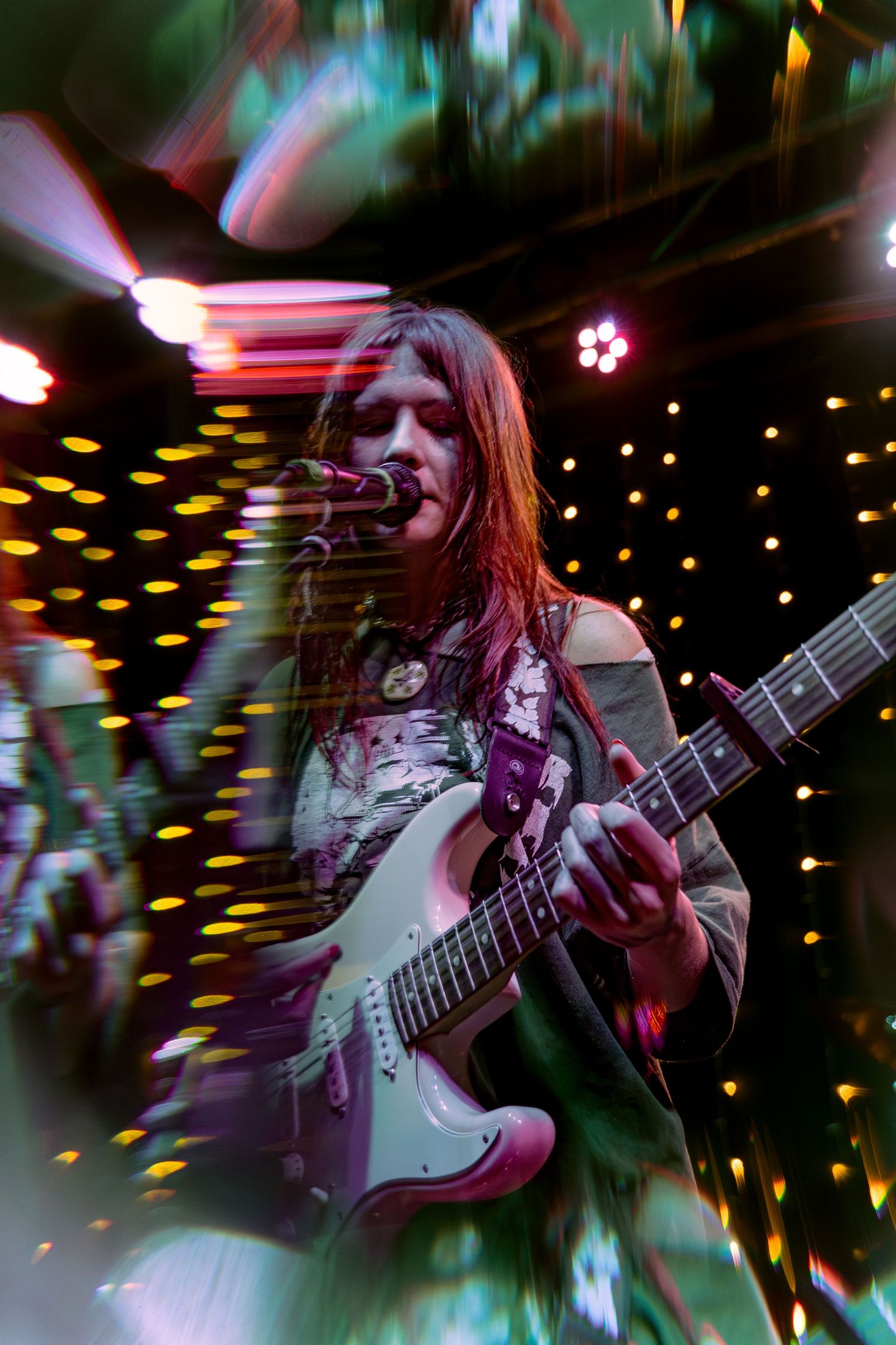 A guitarist performs in a dimly lit venue with twinkling lights creating a dreamy bokeh effect in the background.