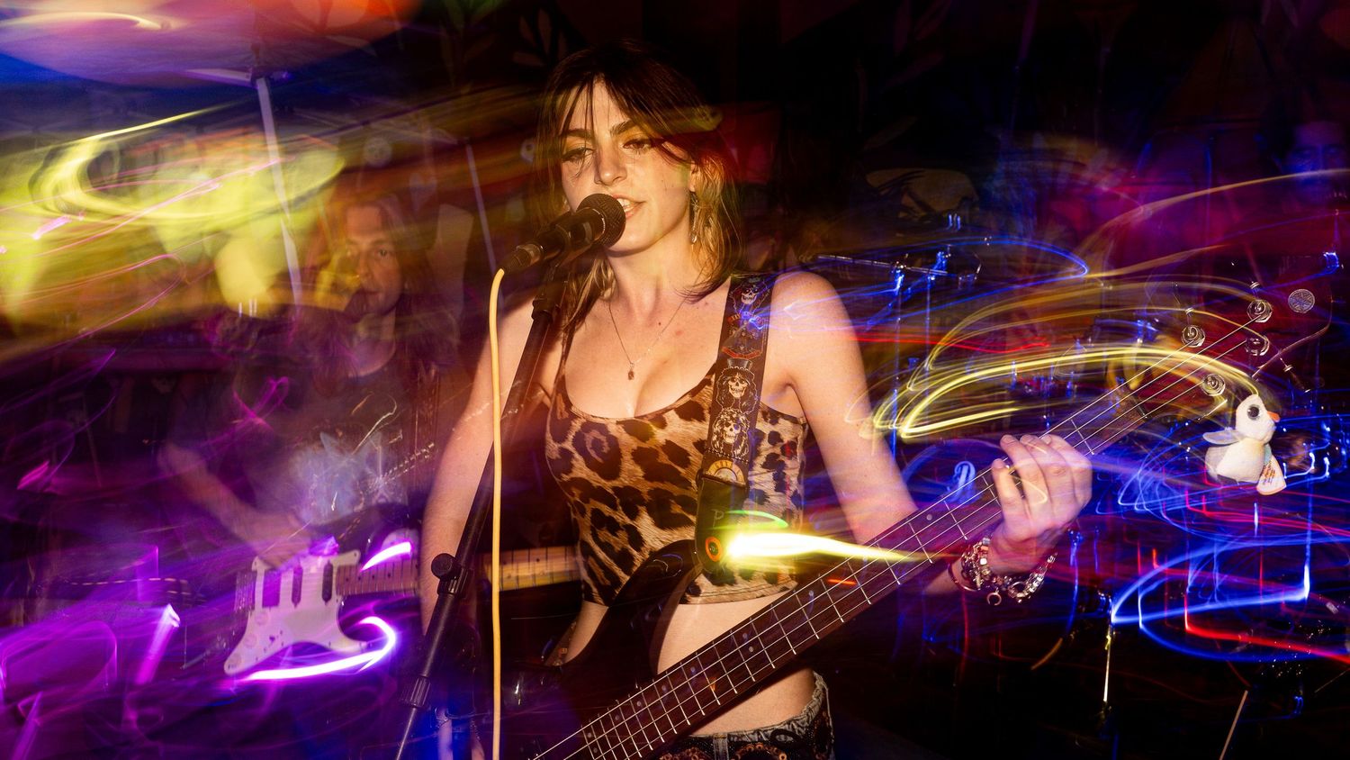 Musician performing with bass guitar under colorful stage lighting and motion effects.